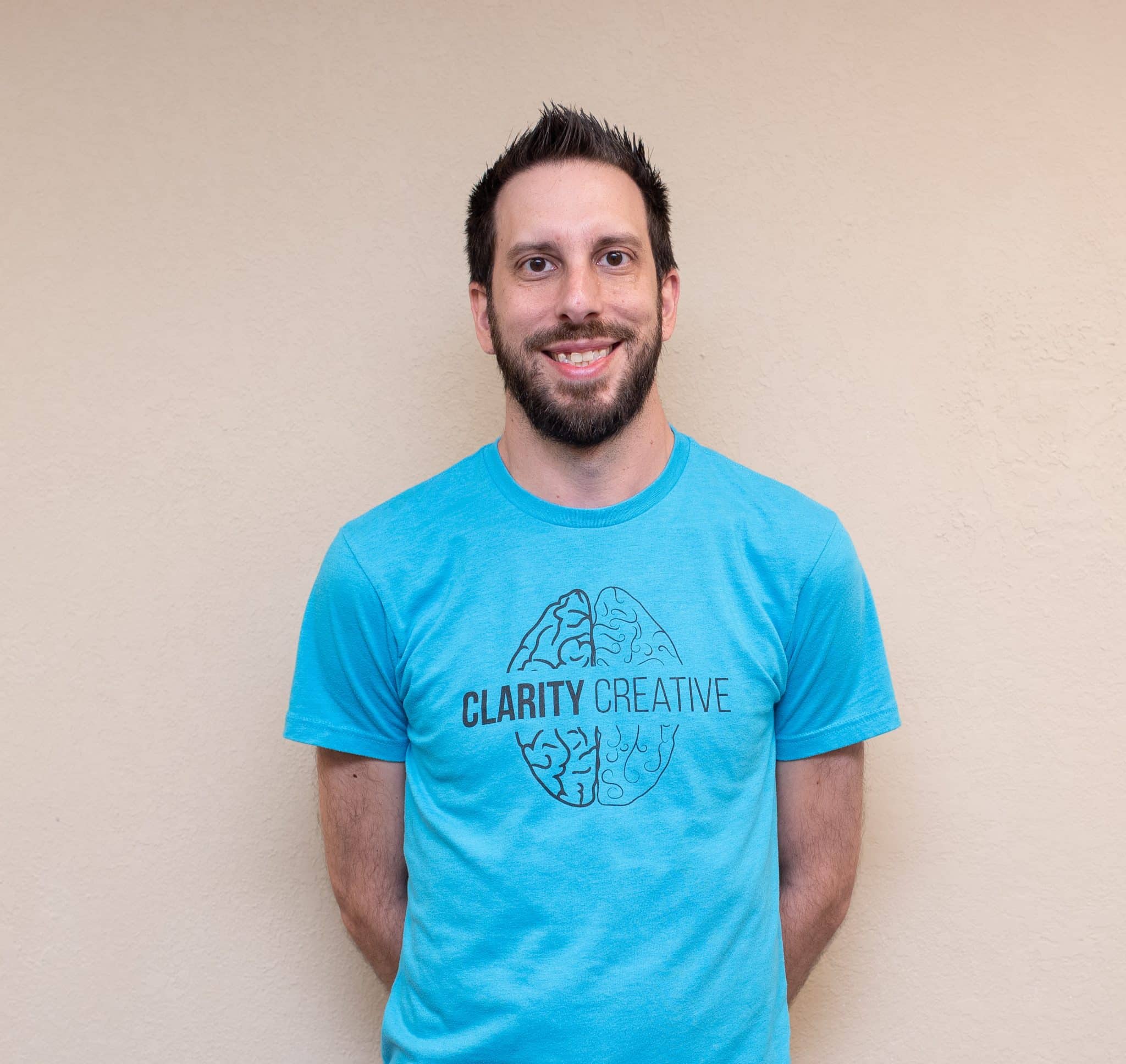 David of Clarity Creative Group. He is smiling, has a teal Clarity Creative shirt and sports a beard and mustache.