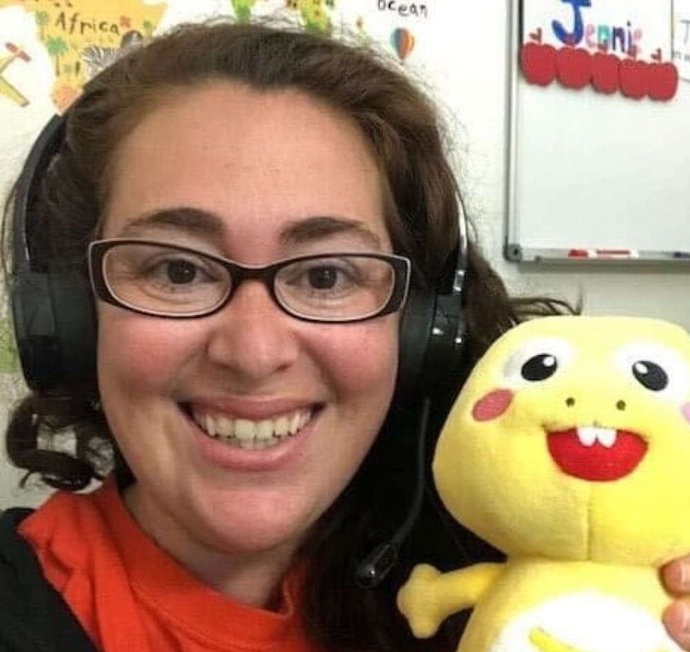 Jennie of Clarity Creative Group. She is wearing headphones, glasses, and holding a stuffed yellow dinosaur.